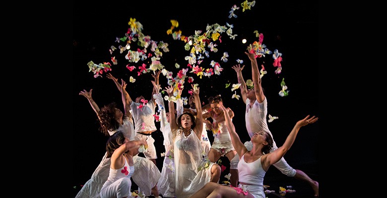 Photo of Dance Brigade performing on stage, in a group throwing flower petals into the air