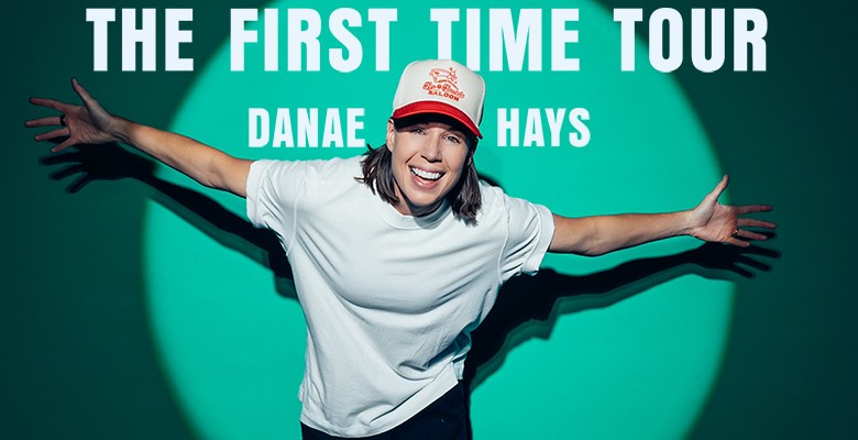 Photo of Danae Hays wearing a baseball hat, white t-shirt, with arms straight to the side, under the spotlight