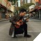 Jake Shimabukuro kneeling in the middle of an empty city street with his ukulele.